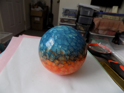 4 inch rouond heavy thick hand blown glass ornament blue and orange flat bottom sits on shelf