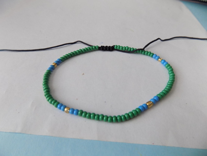 Adjustable bracelet mostly  Green E bead and fewblue and gold on black cord