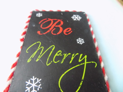 5 inch slate ornament says Be Merry and has snowflakes red and white cord border